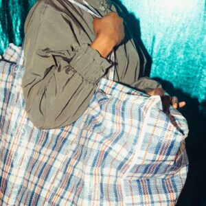 Anonymous black person with large plaid bag standing by blue wall