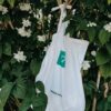 Eco friendly bag with green print hanging on branch of green tree with flowers