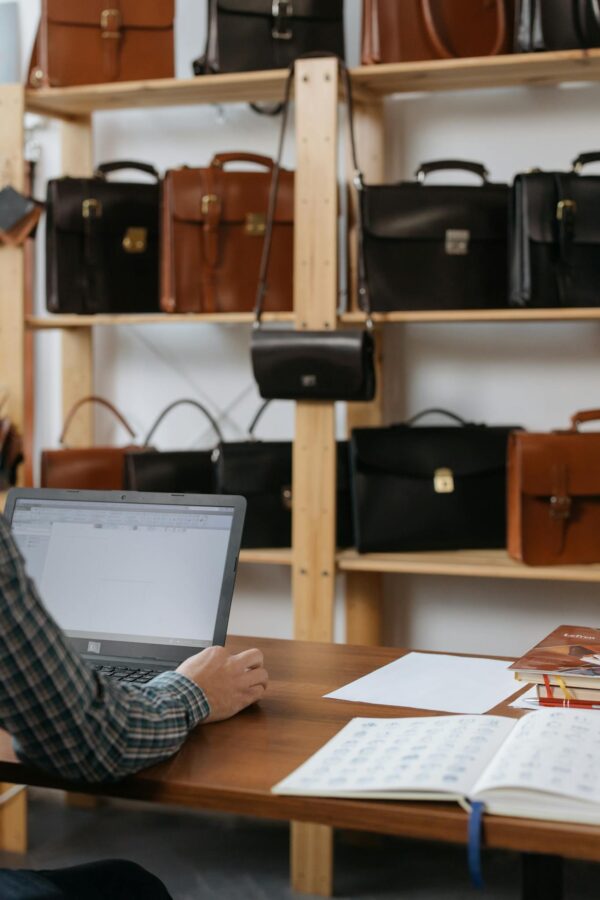 Man Sitting at the Desk with a Laptop in a Store Selling Leather Briefcases and Bags 